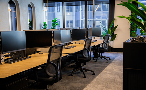 Office interior with oak desks, black task chairs, and multi monitor setups