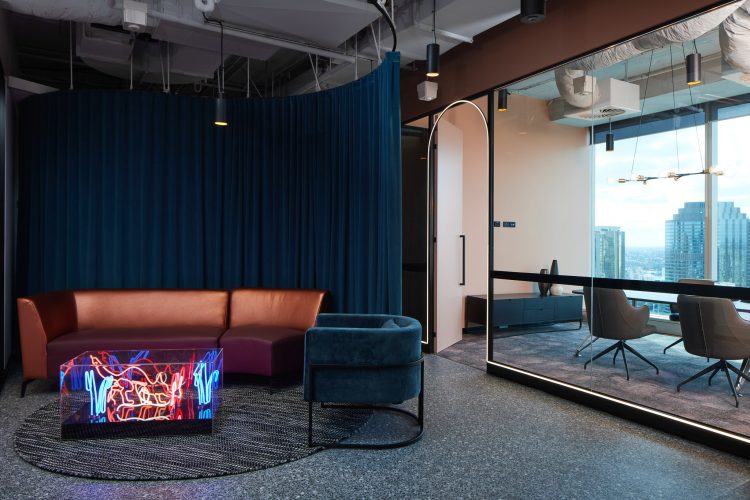 Office lounge area with blue hanging curtains, neon lit coffee table, and meeting room