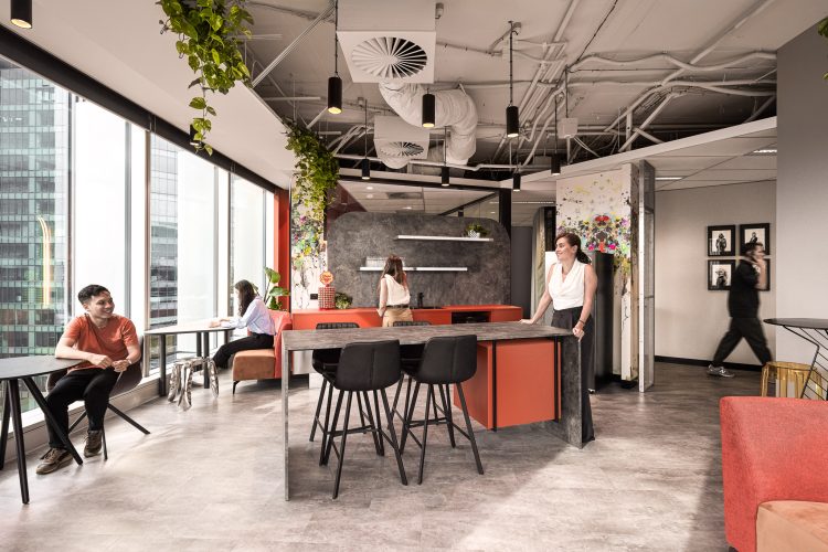 Office kitchen space with smiling employees, stone counter and stools, and dining tables