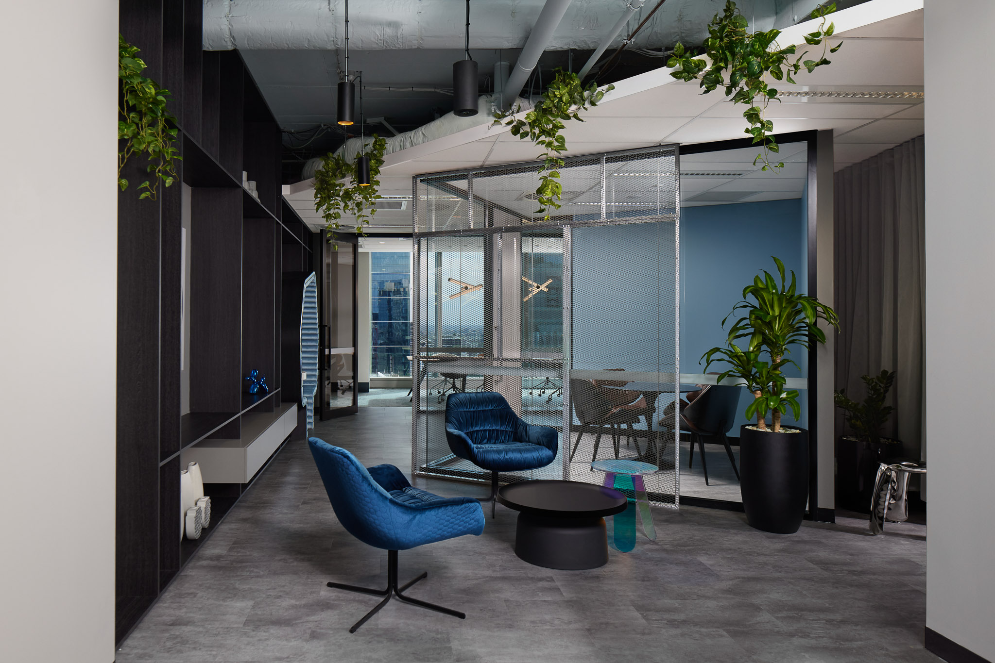 Office breakout space with blue velvet lounge chairs, small black coffee table, and meeting rooms in background